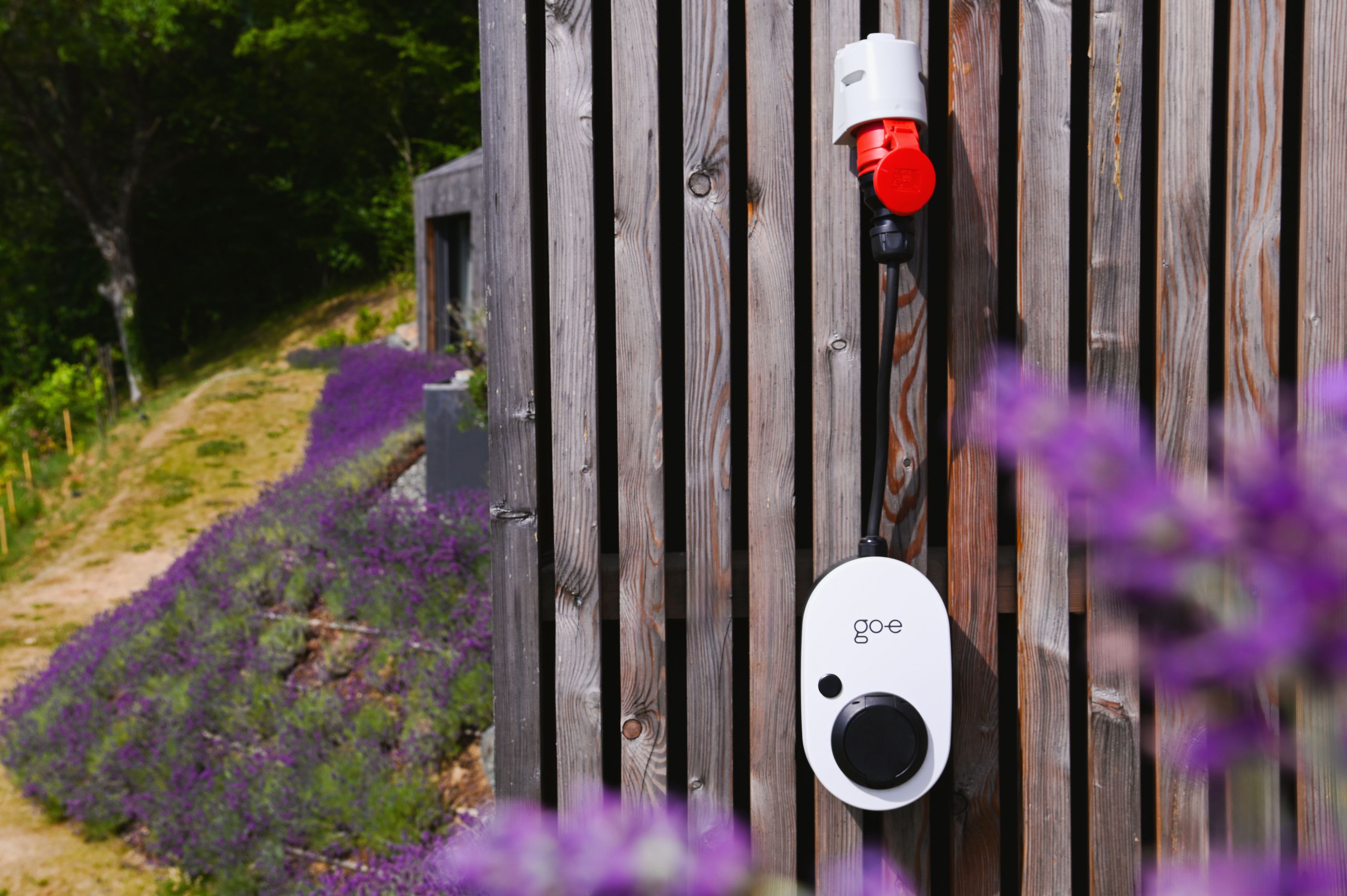 go-e Charger Gemini flex 2.0 monteret på træmur med lavendel — perfekt til sommerhus